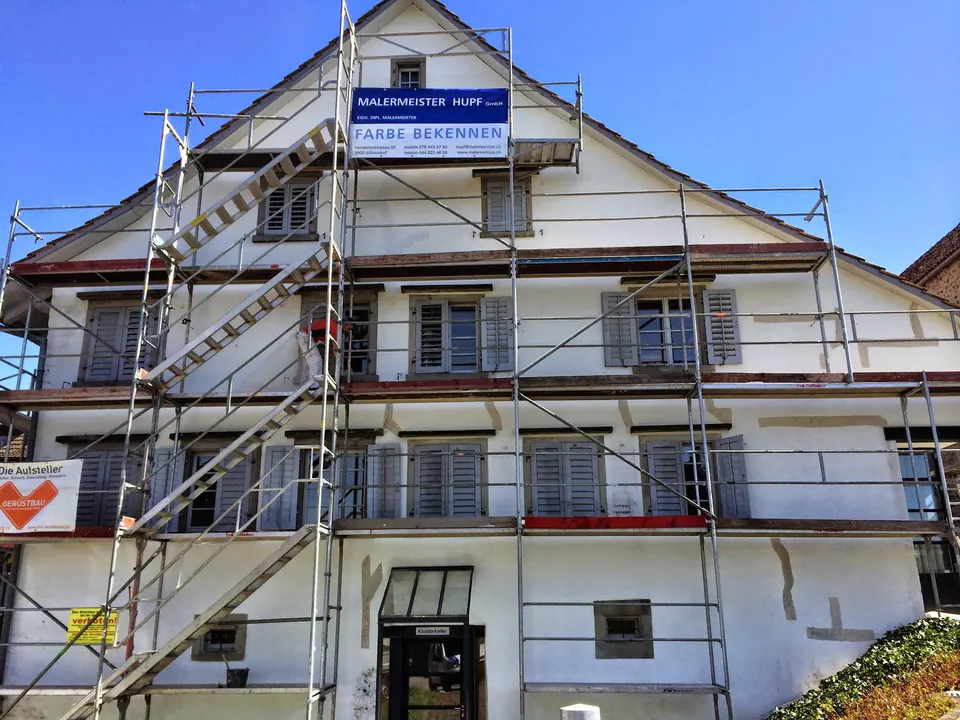 Eingerüstetes Wohnhaus während der Fassadenrenovation, mit Tafel der Malermeister Hupf GmbH