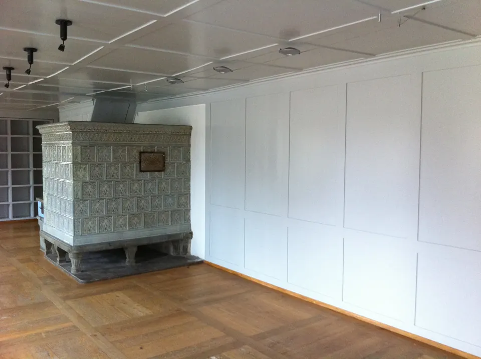 Raum mit weiss gestrichenem Wandtäfer und Kachelofen