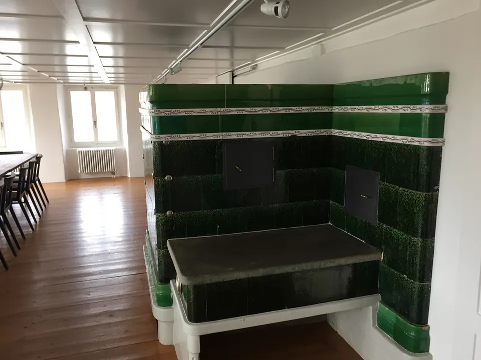 Zimmer mit grünem Kachelofen und hellen Wänden
